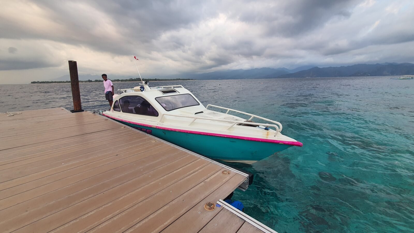 White and turquoise speedboat docked at wooden pier with clear turquoise water and cloudy sky in Lombok
